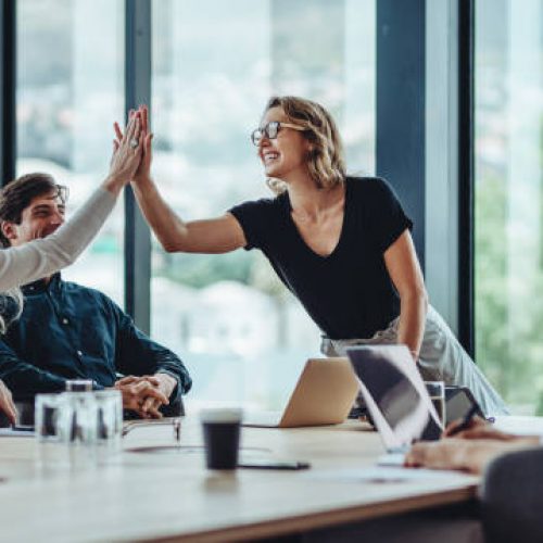 Female professional giving a high five to her colleague in conference room. Group of colleagues celebrating success in a meeting.